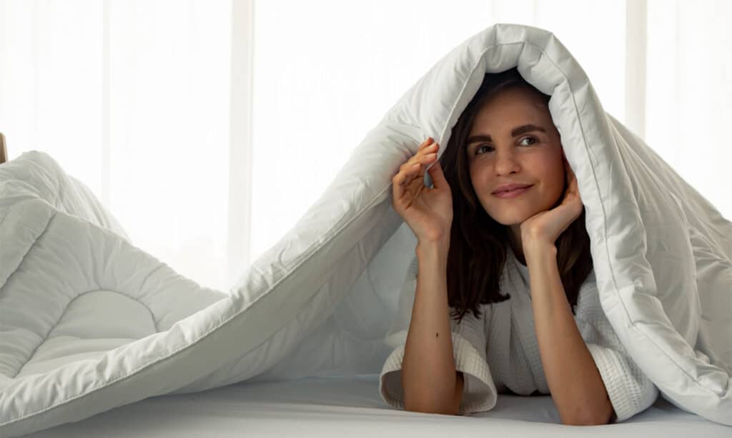 Une femme brune souriante sous sa couette